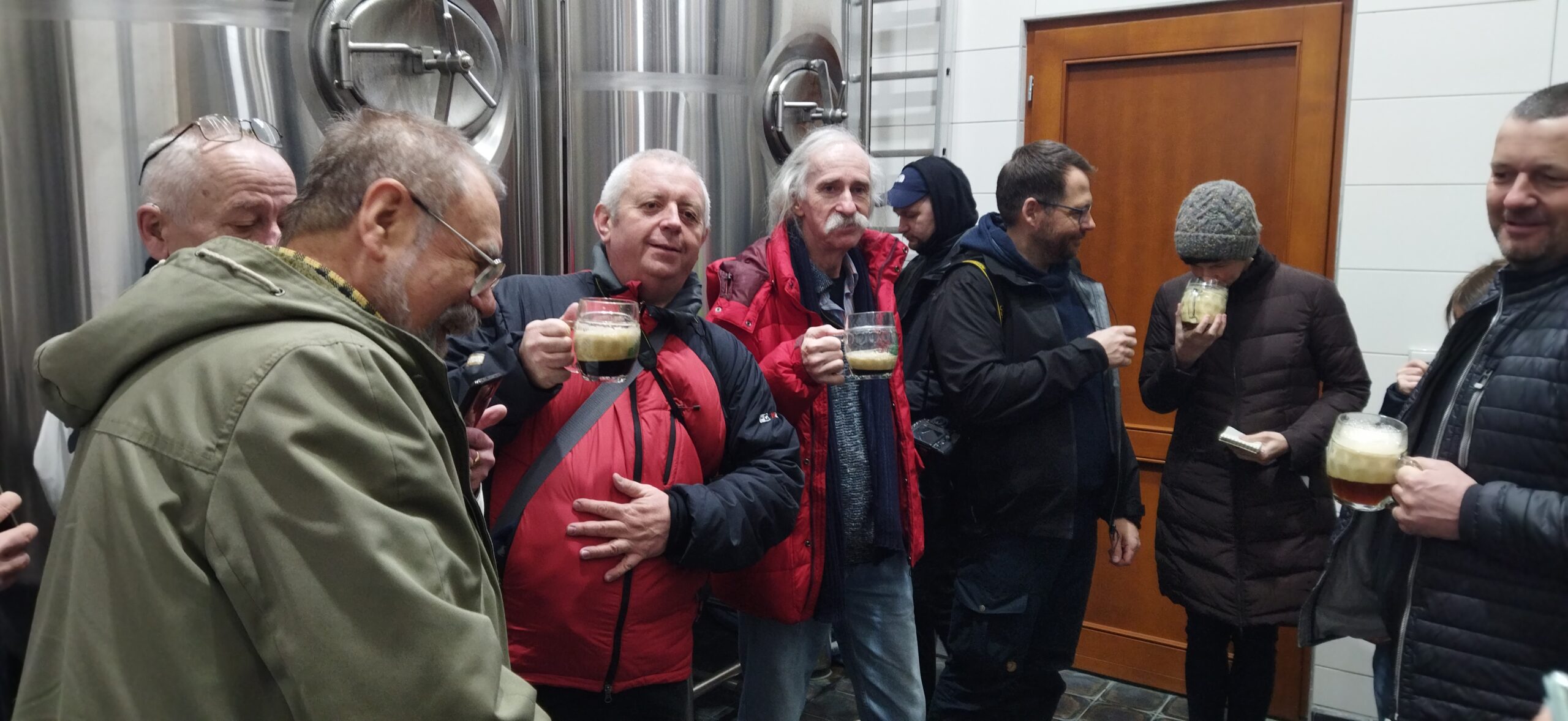 Část polských novinářů stojí u pivního tanku v rámci exkurze. Součástí byla i ochutnávka místního piva.