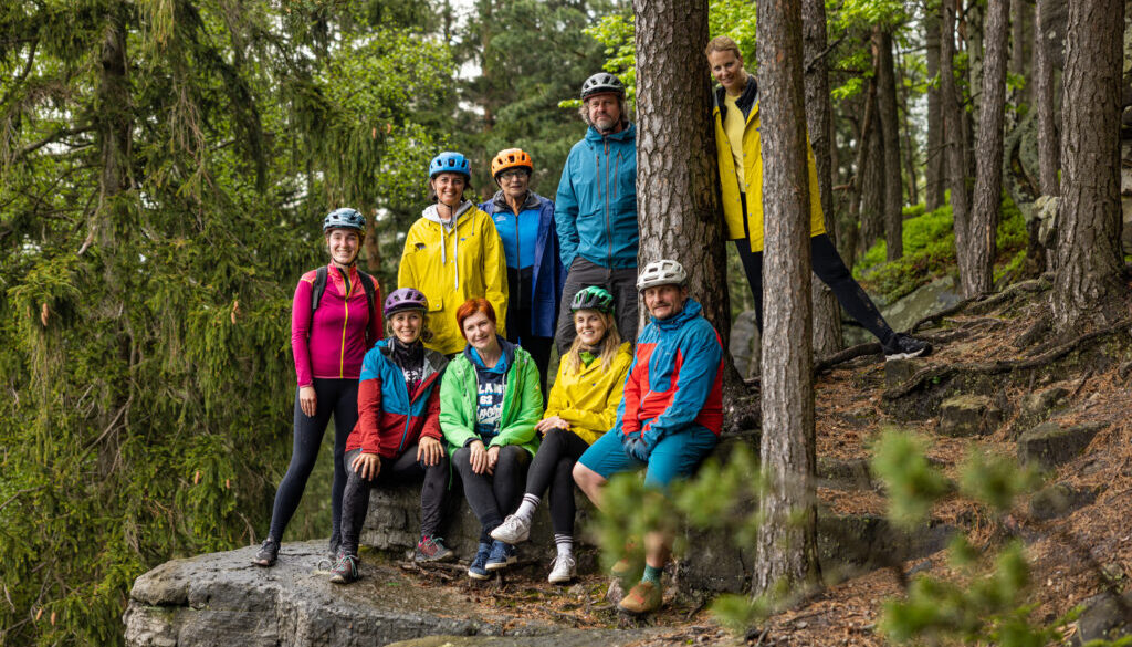 Skupinka novinářů v pestrobarevných bundách v lese před dojezdem na kola.